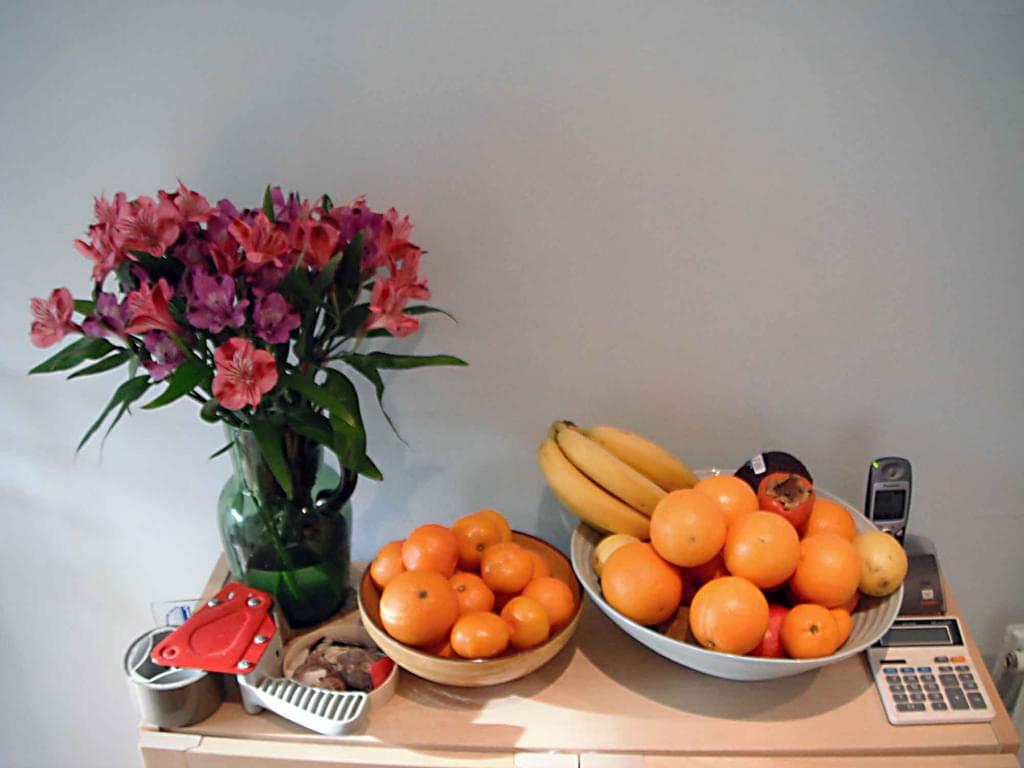 still life of fruit in 2 bowls and vase of flowers in a room